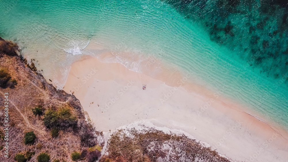 A couple lying on the Pink Beach in Lombok. This place is a hidden gem, not spoiled by tourists. Solitude and calm feelings, waves gently spreading on the beach.