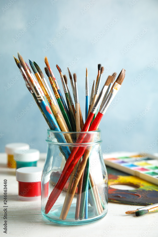 Obraz premium Glass jar with brushes and paints on table against color background