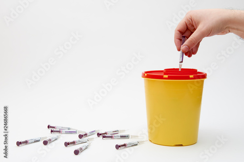 Hand putting needle in safety yellow bin over white background
