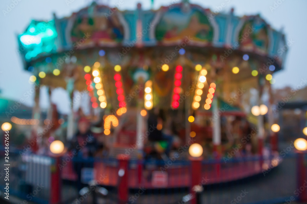 A blurry colorful carousel in the amusement park at evening illumination. The effect of bokeh