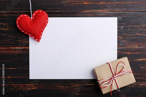 Handmade red felt heart and gift, next to white paper, on wooden table. The concept of St. Valentine and Women's Day, copy space.