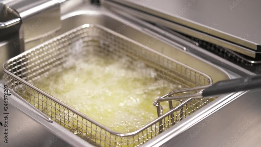 A deep fryer basket with potatoes in a deep fryer container with sizzling oil. A hand in black glove takes the basket out and puts it back A deep fryer basket with potatoes in a deep fryer container with sizzling oil. A hand in black glove takes the basket out and puts it back