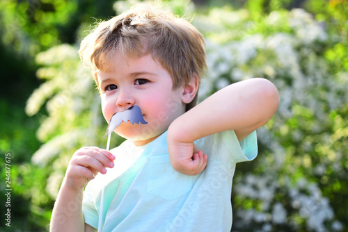 Small child with summer party moustache. Childhood happiness. Childrens day. Little boy child in green forest. spring holiday. Sunny weather. Happy kid in blooming nature. Hot summer photo