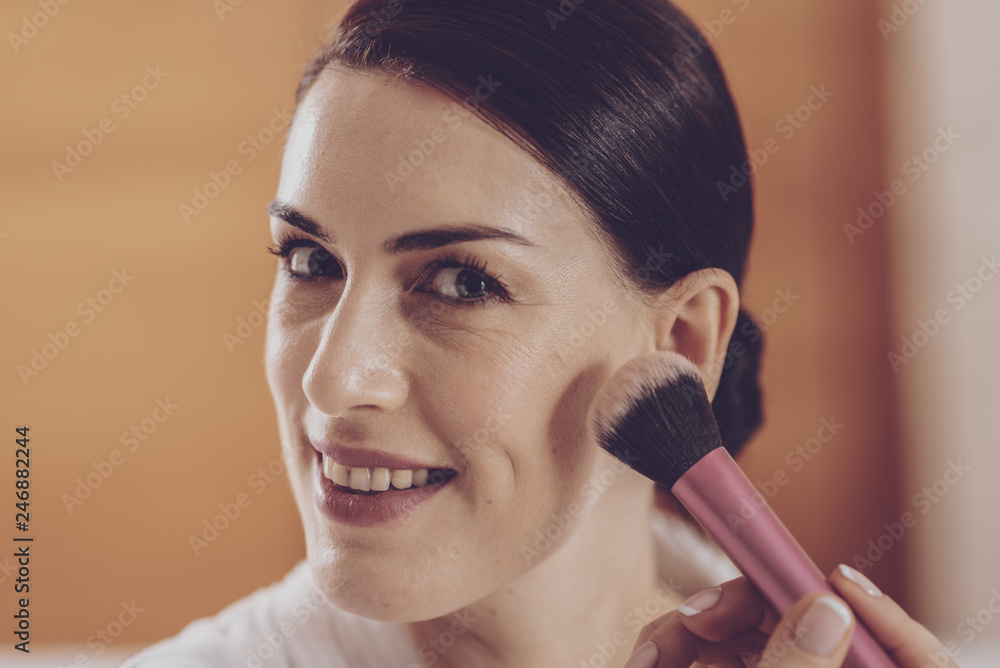 Close up of delighted woman powdering her face Close up of delighted woman powdering her face