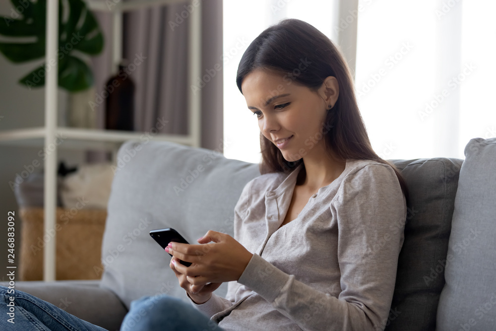 Smiling teen girl using mobile social media app sitting on couch ...