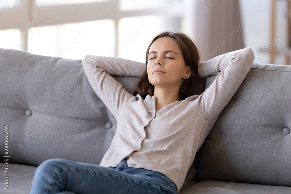 Young calm woman chilling relaxing leaning on comfortable sofa napping on  couch in living room resting
