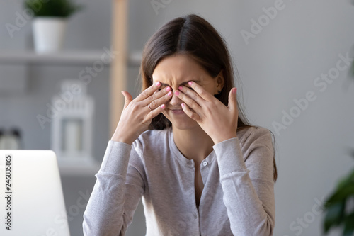 Tired teen girl rubbing dry irritable eyes feel eye strain tension migraine after computer work, exhausted young woman worker student relieving headache pain, bad weak blurry vision, eyesight problem