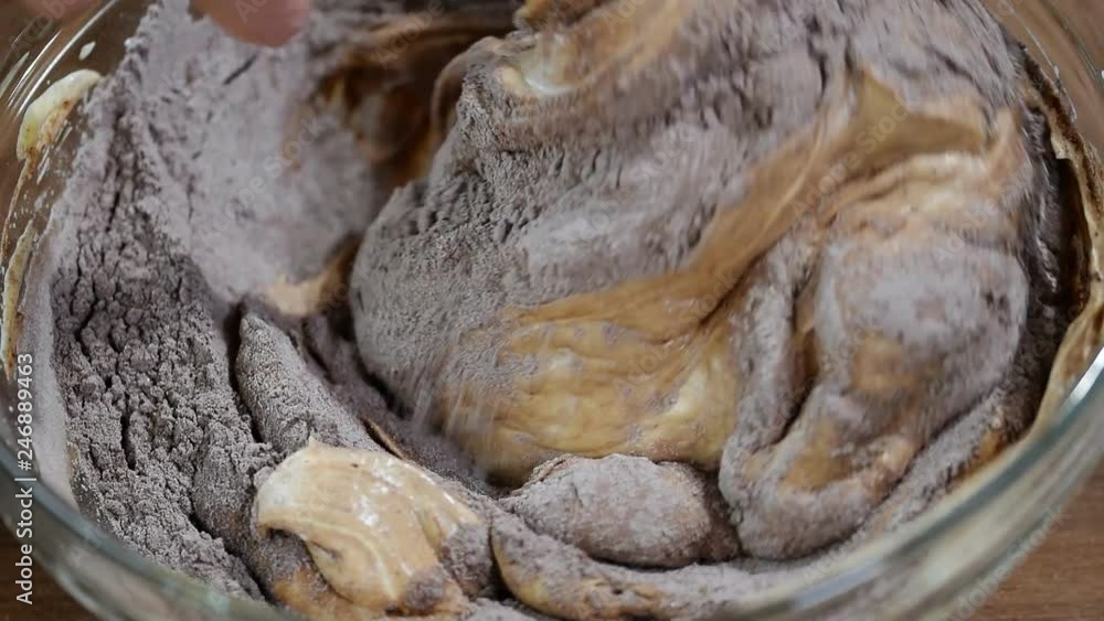 Top view of a female hand with a spatula stirring the chocolate dough in a glass bowl. Top view of a female hand with a spatula stirring the chocolate dough in a glass bowl.