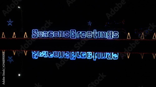 4K Seasons Greetings Neon Sign On Water With Water Ripples And Neon Christmas Trees Pan Full Left To Right photo