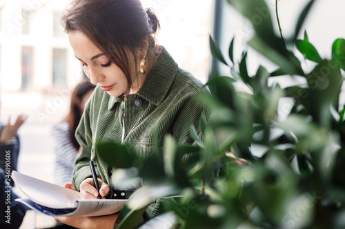 Woman stand at office surround with green plants and write at her note book