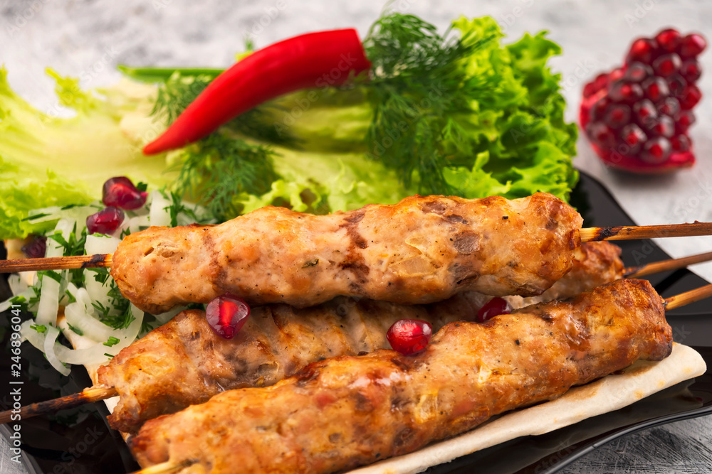 Minced meat kebab with spices. Baked meat. Hot red pepper. Garnish of lettuce, dill and pomegranate. Close up.