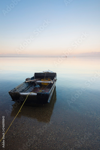 Beautiful seascape with a single boat reflected in the still ocean at sunrise