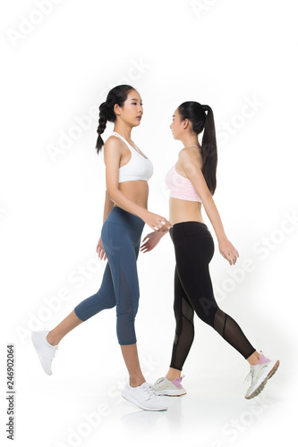 Two Asian Tan Skin Fitness women exercise wear pink blue black bra pant suit gear jump walk cross in the air white background, studio lighting copy space isolated, concept 2 Woman motion blur hands
