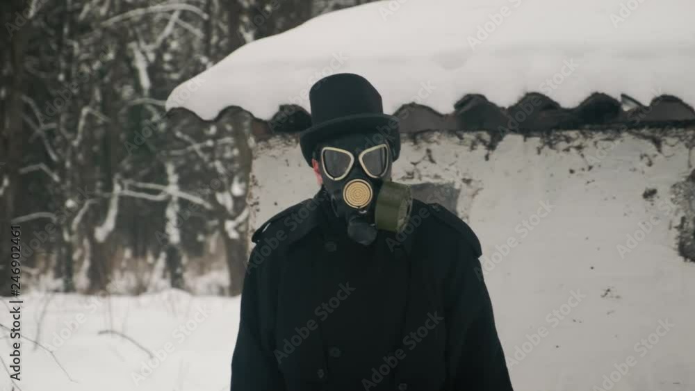 Middle view sho: A character in a gas mask stands near an abandoned barn and looks eerily into the camera. 60fps. 4k Middle view sho: A character in a gas mask stands near an abandoned barn and looks eerily into the camera. 60fps. 4k