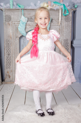 Portrait of cute european little blonde princess girl with crown in beautiful dress in decorated studio in christmas location with toys and christmas tree