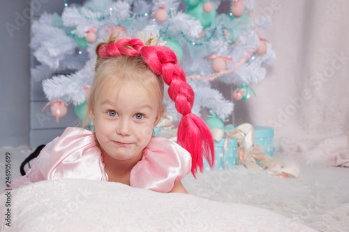 Portrait of cute european little blonde princess girl with crown in beautiful dress in decorated studio in christmas location with toys and christmas tree