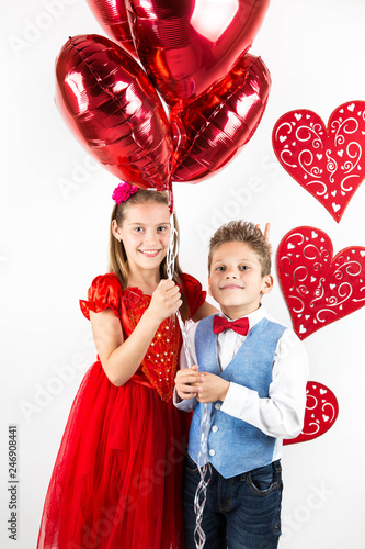 Saint Valentine's day. Pretty girl with red dress and gentleman boy with blue vest, red butterfly tie,  red roses bucket and heart shaped gift box. Valentines day kids. Love and friendship. Woman Day