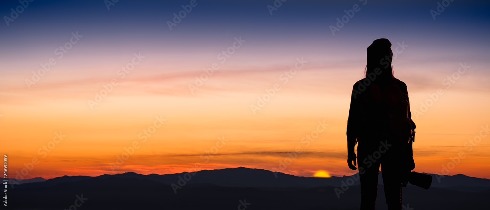 Back view of young hipster photographer holding the camera with sunret on mountain natural background.
