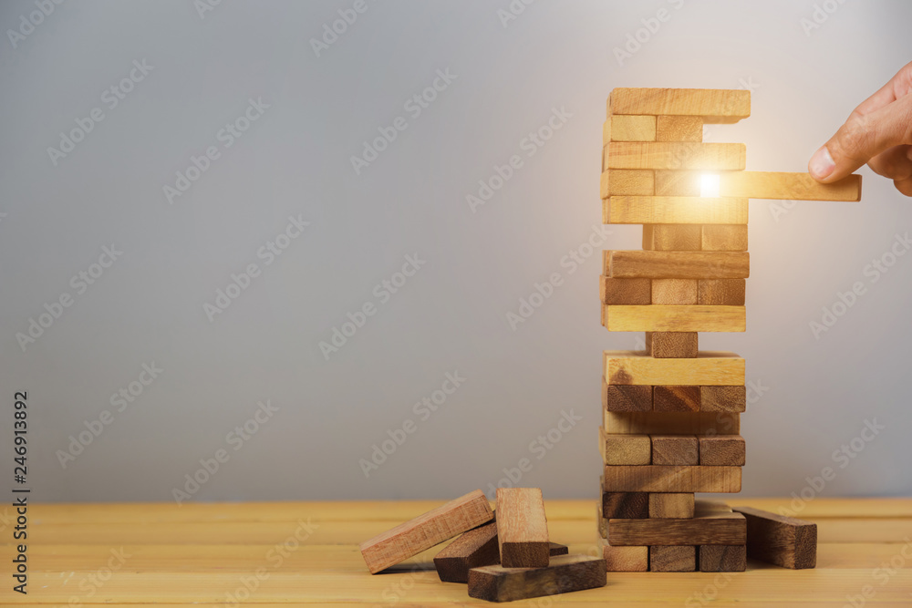 Hand of businessman pulling out or placing wood block on the tower, plan and strategy in business.for background - Image Hand of businessman pulling out or placing wood block on the tower, plan and strategy in business.for background - Image