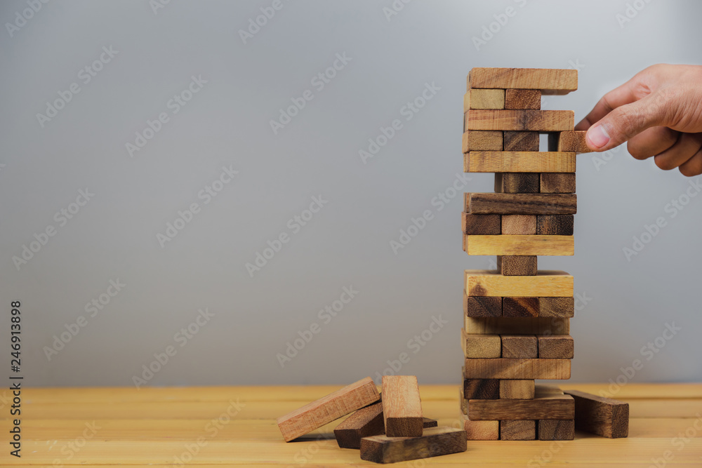 Hand of businessman pulling out or placing wood block on the tower, plan and strategy in business.for background - Image Hand of businessman pulling out or placing wood block on the tower, plan and strategy in business.for background - Image