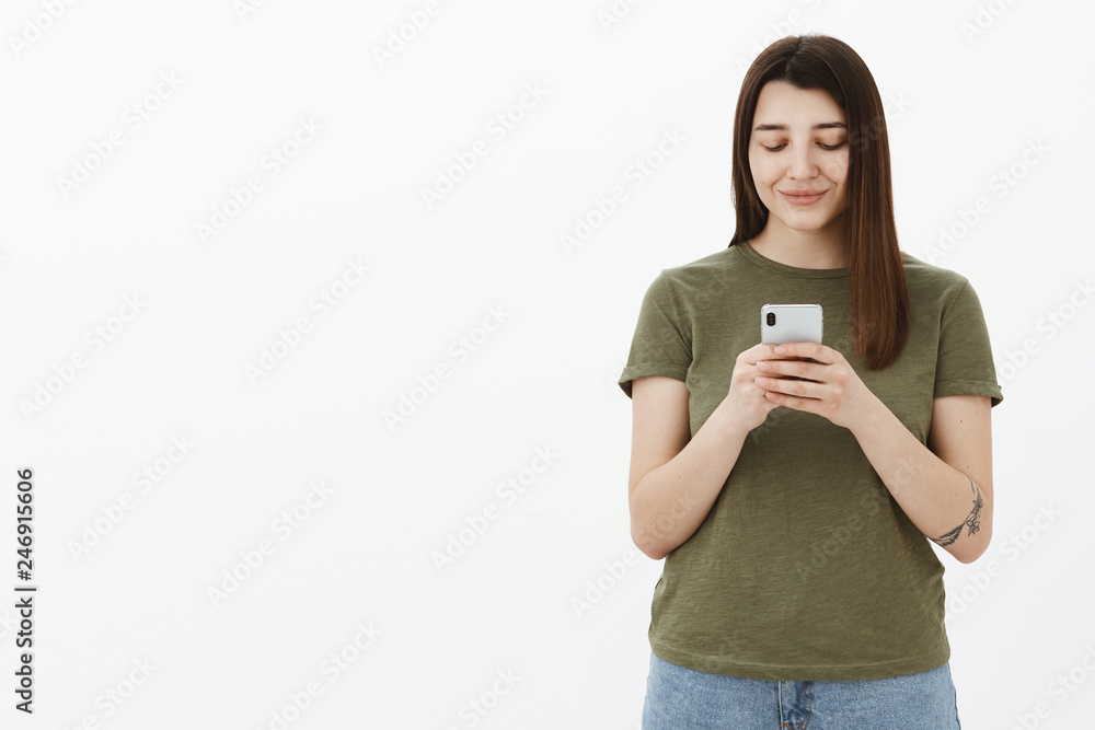 Girlfriend additing pictures on smartphone while waiting for date in cafe, standing delighted and happy over white background smiling at mobile phone screen, texting or messaging over gray wall Girlfriend additing pictures on smartphone while waiting for date in cafe, standing delighted and happy over white background smiling at mobile phone screen, texting or messaging over gray wall