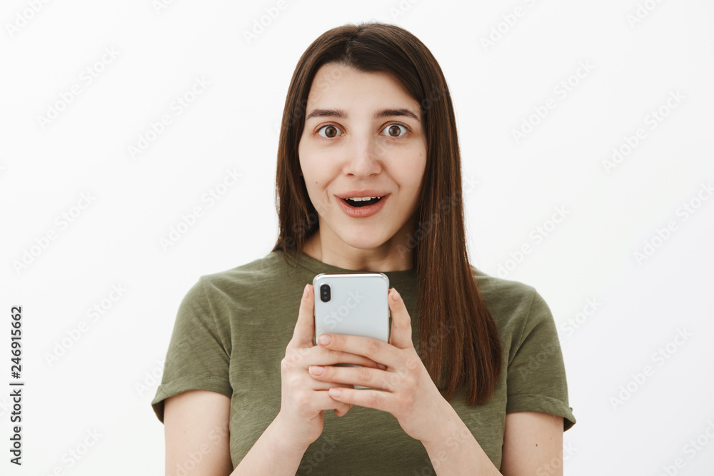 So cool best phone ever. Portrait of impressed and fascinated happy speechless brunette in 20s holding smartphone and smiling astonished at camera as excited of cellphone features over gray wall So cool best phone ever. Portrait of impressed and fascinated happy speechless brunette in 20s holding smartphone and smiling astonished at camera as excited of cellphone features over gray wall