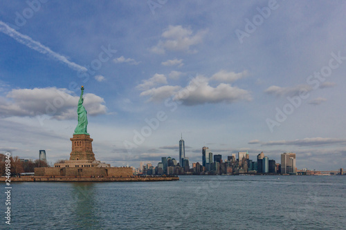 Statue of Liberty overlooking buildings of downtown Manhattan by water, in New York City, USA