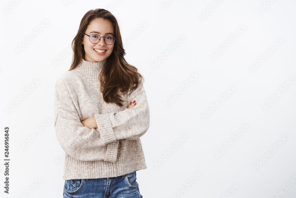 Studi shot of stylish creative and happy young european woman in glasses with perfect smile holding hands crossed over chest in confident upbeat pose, wearing warm sweater in cold winter day Studi shot of stylish creative and happy young european woman in glasses with perfect smile holding hands crossed over chest in confident upbeat pose, wearing warm sweater in cold winter day
