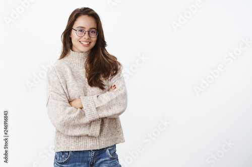 Studi shot of stylish creative and happy young european woman in glasses with perfect smile holding hands crossed over chest in confident upbeat pose, wearing warm sweater in cold winter day