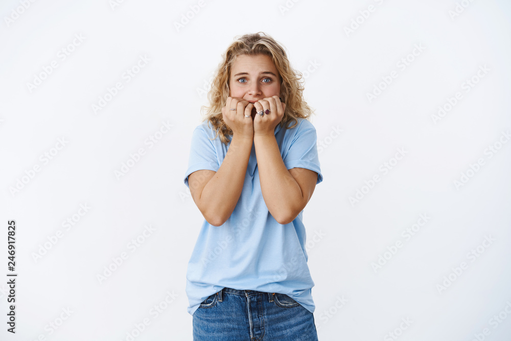Girl scared being home alone. Potrait of cute insecure young woman biting fingernails and shaking, having goosebumps from fear widen eyes as standing horrified over white background Girl scared being home alone. Potrait of cute insecure young woman biting fingernails and shaking, having goosebumps from fear widen eyes as standing horrified over white background