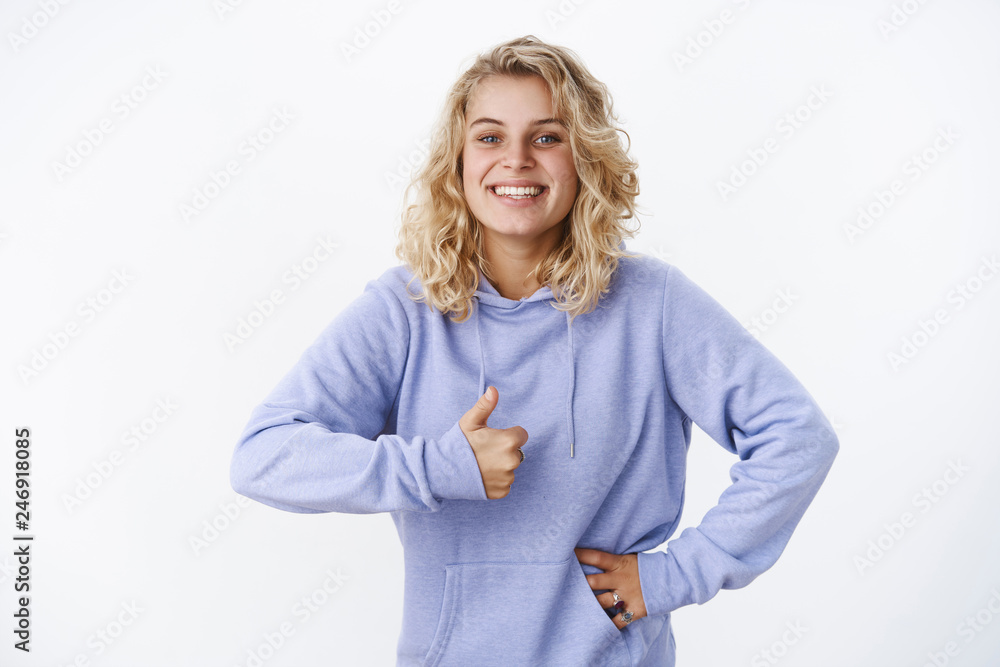 Obraz premium Girl agrees showing thumb up and smiling happily absolutely liking awesome new haircut grinning from joy holding hand on waist and making approval, recommend gesture over white wall