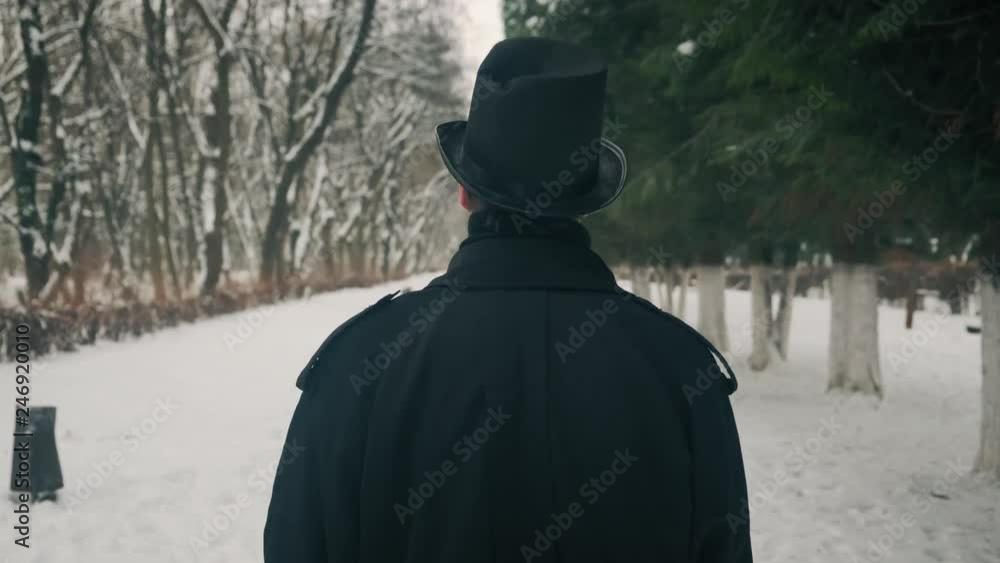 Middle view shot: A man in a black cloak and hat walks in the park alley. 60fps. 4k Middle view shot: A man in a black cloak and hat walks in the park alley. 60fps. 4k