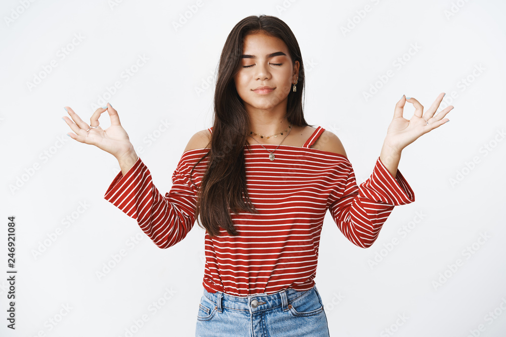 Waist-up shot of calm and relieved charming young teenage indian girl in blouse standing in meditating pose with closed eyes and hands raised sideways with nirvana orbs over gray background Waist-up shot of calm and relieved charming young teenage indian girl in blouse standing in meditating pose with closed eyes and hands raised sideways with nirvana orbs over gray background