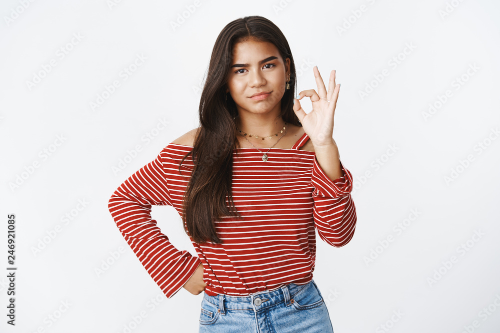 Portrait of gloomy displeased teenage girl saying okay and showing ok gesture but feeling dissatisfied and upset, making childish upset grimace as unwilling do housework over gray wall Portrait of gloomy displeased teenage girl saying okay and showing ok gesture but feeling dissatisfied and upset, making childish upset grimace as unwilling do housework over gray wall