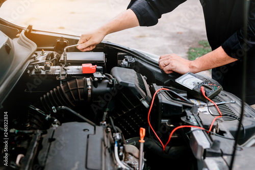 Car mechanic is checking the engine and holding the battery gauge.