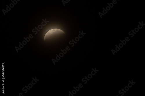 Fototapeta Naklejka Na Ścianę i Meble -  Full Lunar Eclipse in January 2019 is pictured in various stages of the eclipse. The bright white moon turns dark and black and eventually a yellowish orange that glows in the dark night sky