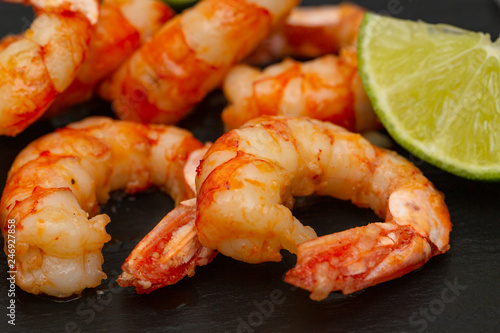 Tasty appetizing roasted shrimps prawns with lime on black background. 