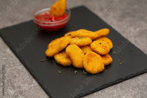 Fried crispy chicken nuggets with ketchup on black board.
