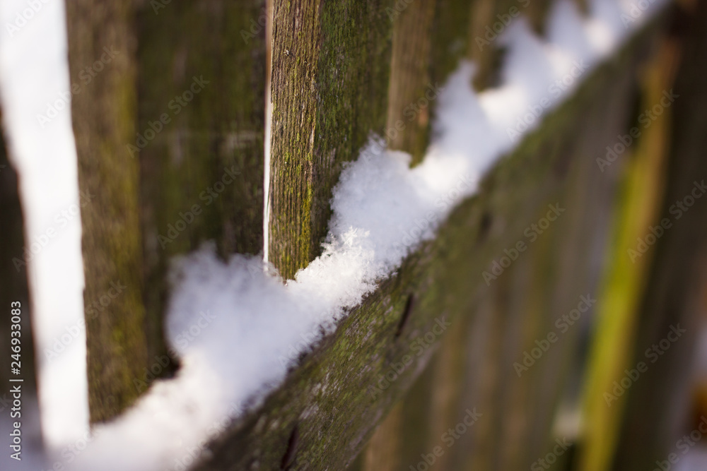 Fluffy snow lies on the fence on a sunny winter day. The sun's rays shine through the openings in the fence Fluffy snow lies on the fence on a sunny winter day. The sun's rays shine through the openings in the fence