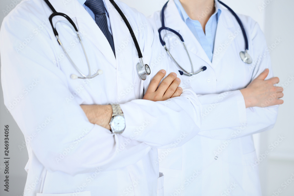 Team of unknown doctors standing straight with arms crossed in hospital. Physicians ready to help. Healthcare, insurance and medicine concept Team of unknown doctors standing straight with arms crossed in hospital. Physicians ready to help. Healthcare, insurance and medicine concept