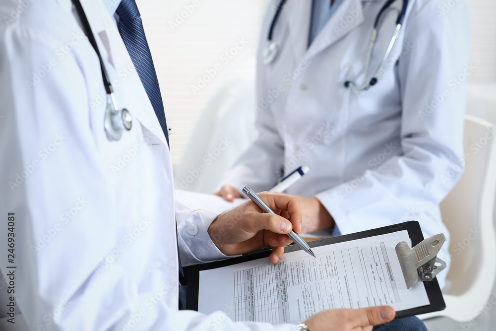 Two unknown doctors filling up medical form on clipboard, just hands closeup. Physicians asking question to patient or discussing medication program. Healthcare, insurance and medicine concept Two unknown doctors filling up medical form on clipboard, just hands closeup. Physicians asking question to patient or discussing medication program. Healthcare, insurance and medicine concept
