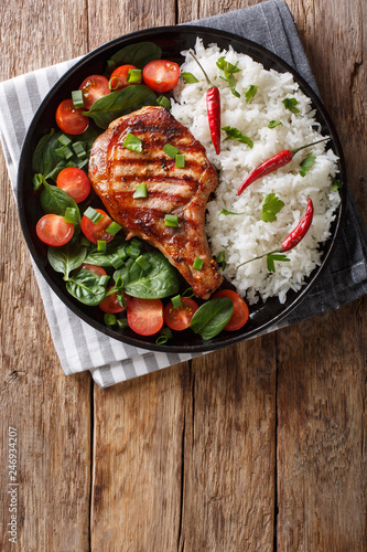 Grilled pork steak with rice garnish and fresh vegetable salad close-up. Vertical top view photo