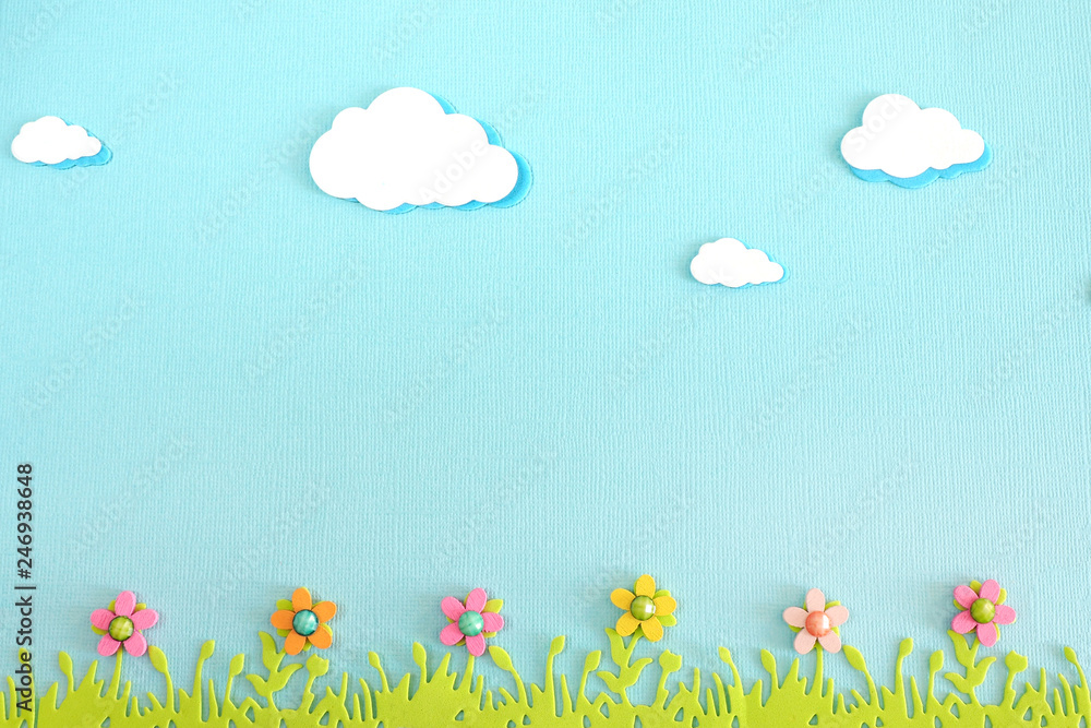 appliqué clouds, grass and wooden flowers on blue textured paper. copy space.. appliqué clouds, grass and wooden flowers on blue textured paper. copy space..