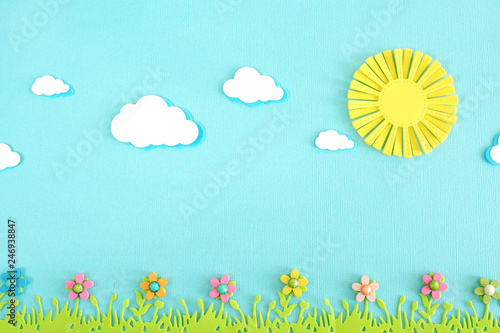 appliqué yellow sun, clouds, lush green grass and bright multicolored wooden flowers on a blue background.