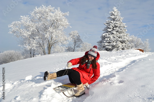 Happy young beautiful woman in a bright red jacket, hat and scarf on a sled on the background of a fabulous winter landscape on the mountain 