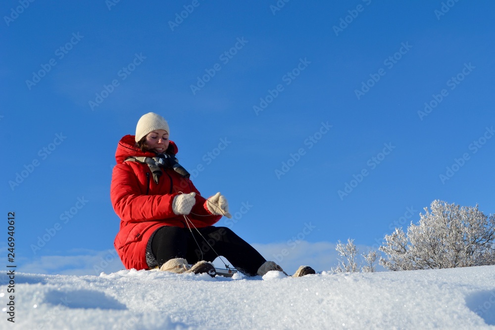 Happy young beautiful woman in a bright red jacket, hat and scarf on a sled on the background of a fabulous winter landscape on the mountain Happy young beautiful woman in a bright red jacket, hat and scarf on a sled on the background of a fabulous winter landscape on the mountain