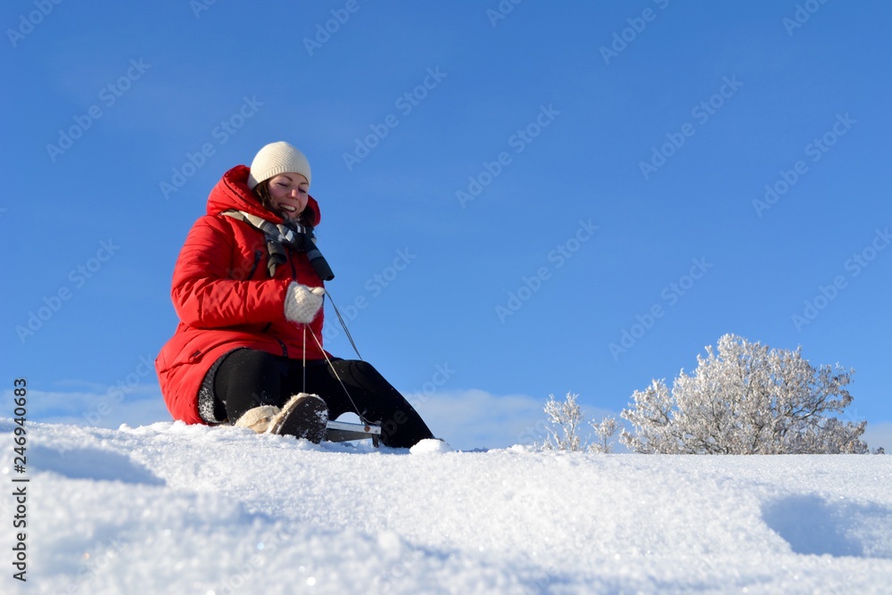 Happy young beautiful woman in a bright red jacket, hat and scarf on a sled on the background of a fabulous winter landscape on the mountain Happy young beautiful woman in a bright red jacket, hat and scarf on a sled on the background of a fabulous winter landscape on the mountain
