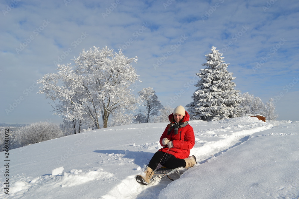 Happy young beautiful woman in a bright red jacket, hat and scarf on a sled on the background of a fabulous winter landscape on the mountain 