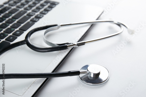Modern medical technology and sofware advances concept. Doctor's working table with stethoscope acoustic device, laptop computer keyboard close up. Copy space, background, top view, flat lay.