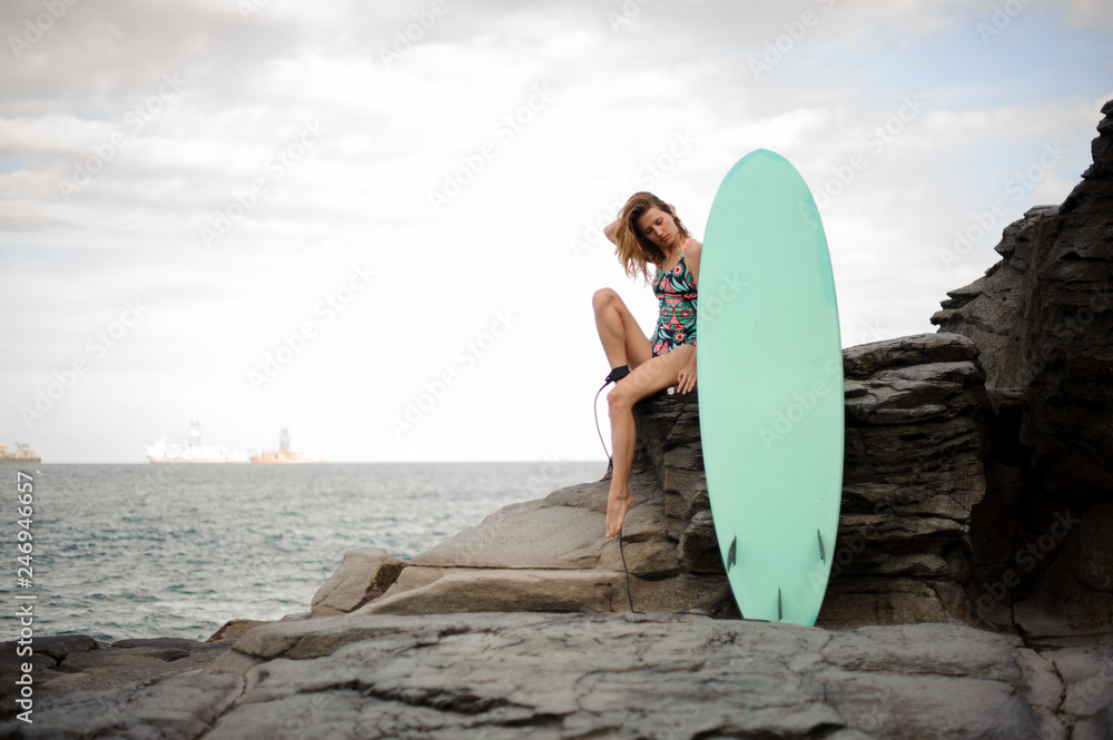 Beautiful girl in the multi colored swimsuit sitting with the surf on the rock